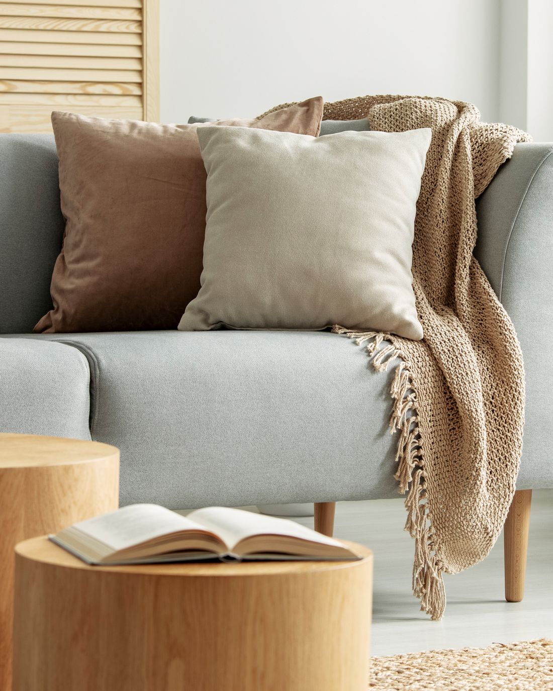 Close-up of a beige pillow and a knit throw with fringe on a light gray sofa.
